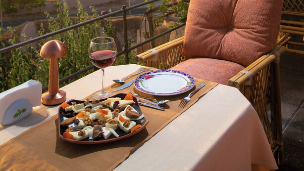 Une table à manger dressée avec une assiette de nourriture, un verre à vin et une chaise dotée d’un coussin, offrant une vue sur un paysage pittoresque.