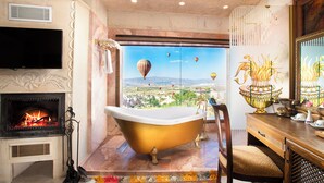 A bathroom with a freestanding bathtub, a fireplace, and a large window with a view of hot air balloons.