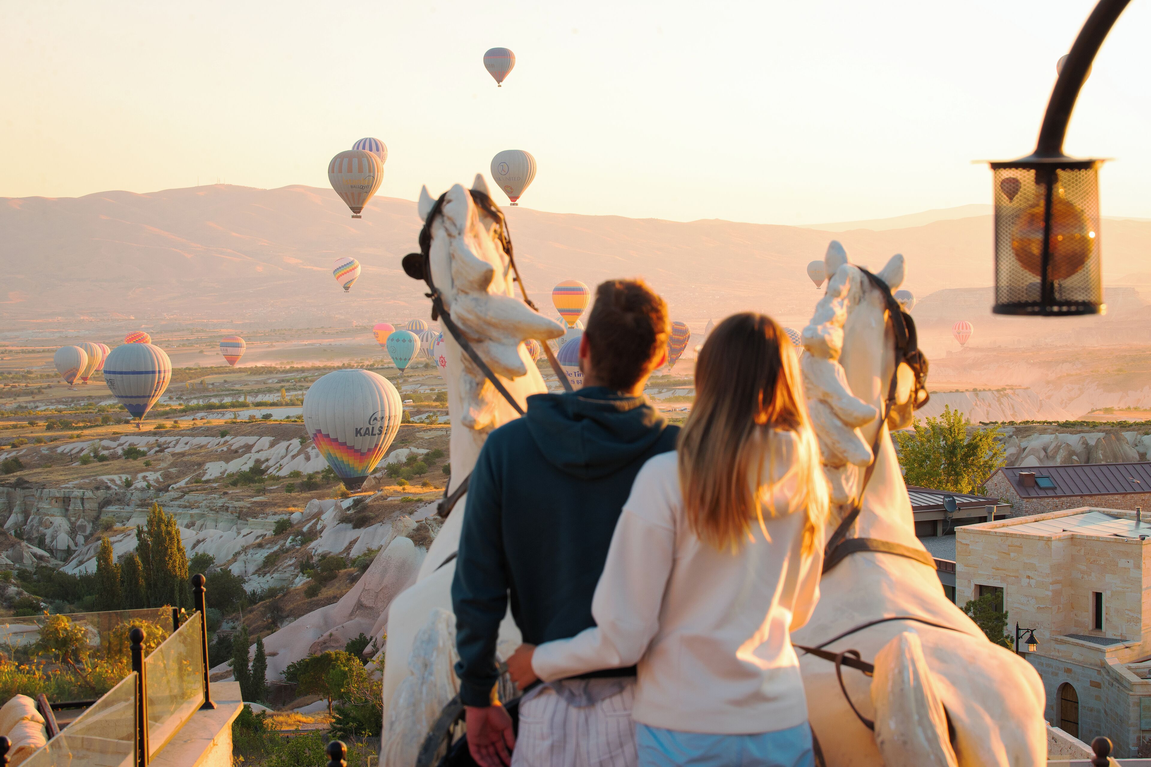 A couple on horseback overlooking a landscape with hot air balloons and a mountainous backdrop.