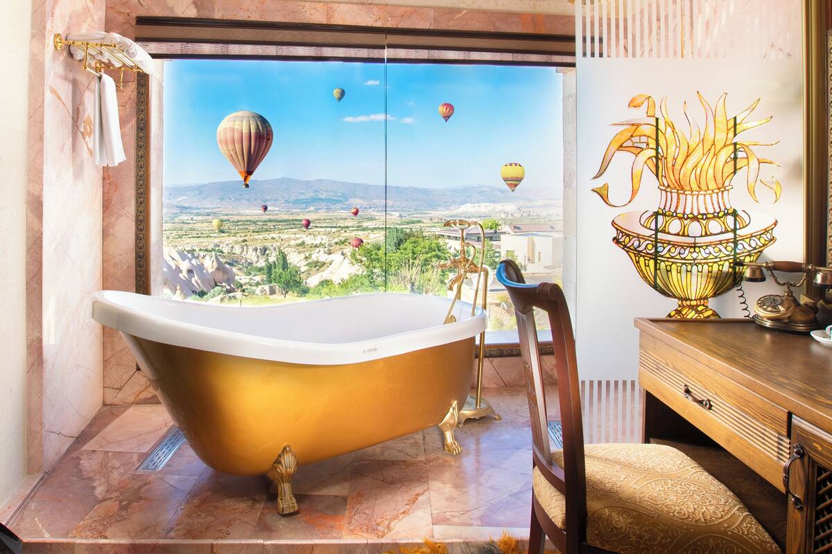 Une salle de bain dotée d’une baignoire sur pieds, d’un meuble-lavabo en bois et d’une grande fenêtre offrant une vue sur un paysage et des montgolfières.