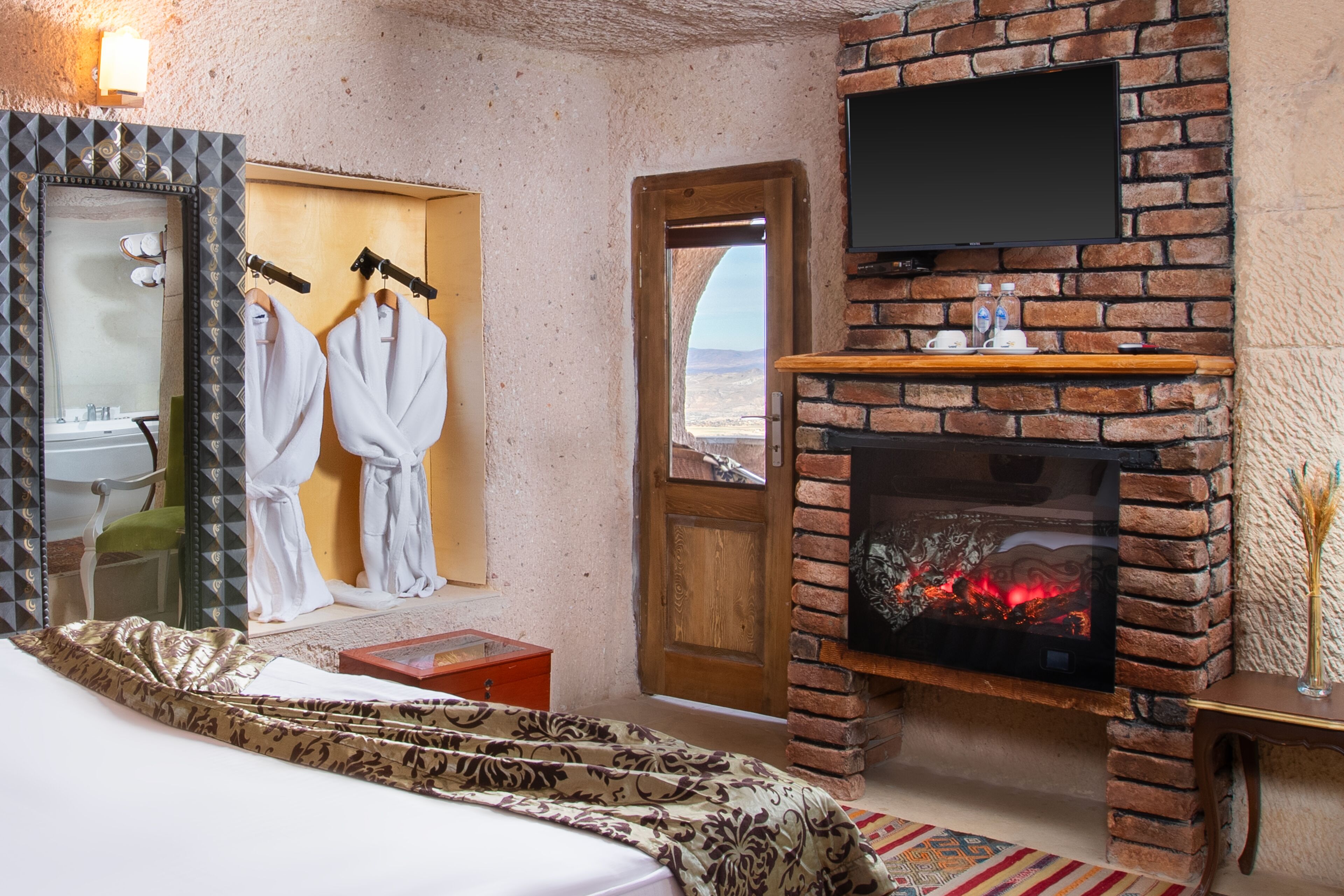 Habitación de hotel con chimenea de ladrillo, un televisor montado encima y un espejo grande con un marco geométrico.