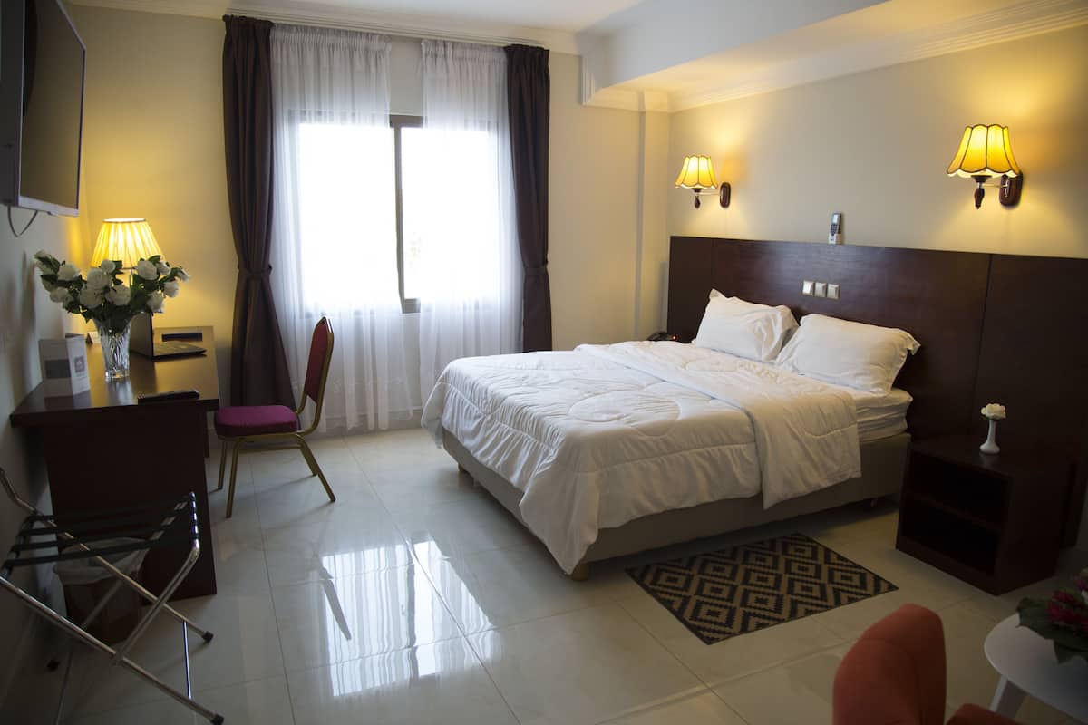 Een hotelkamer met een bed, een bureau, een stoel, een lamp en een raam met gordijnen.