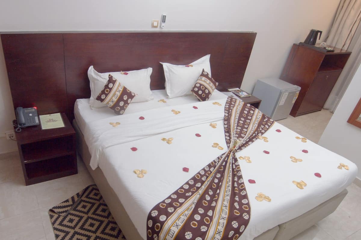 Een net opgemaakt bed met beddengoed met een patroon, een nachtkastje met een telefoon en een klein plankje.