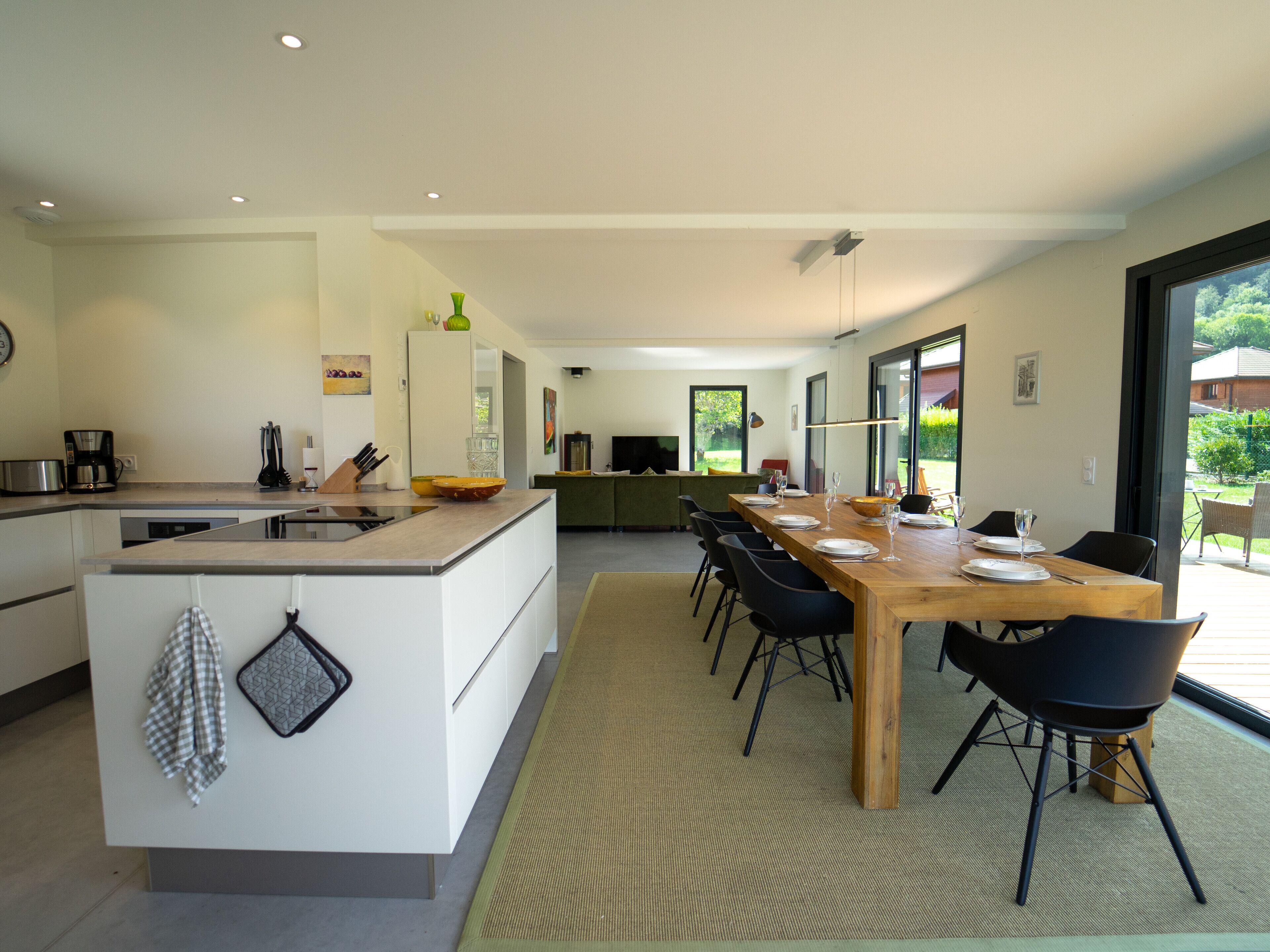 A modern kitchen with a central island, dining table with chairs, and a view of the outdoors.