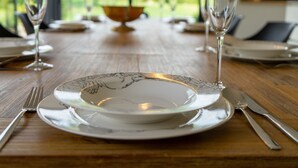 A dining table with a white plate, a fork, a knife, and two wine glasses.
