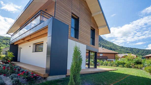 A modern two-story house with a sloped roof, large windows, and a balcony.