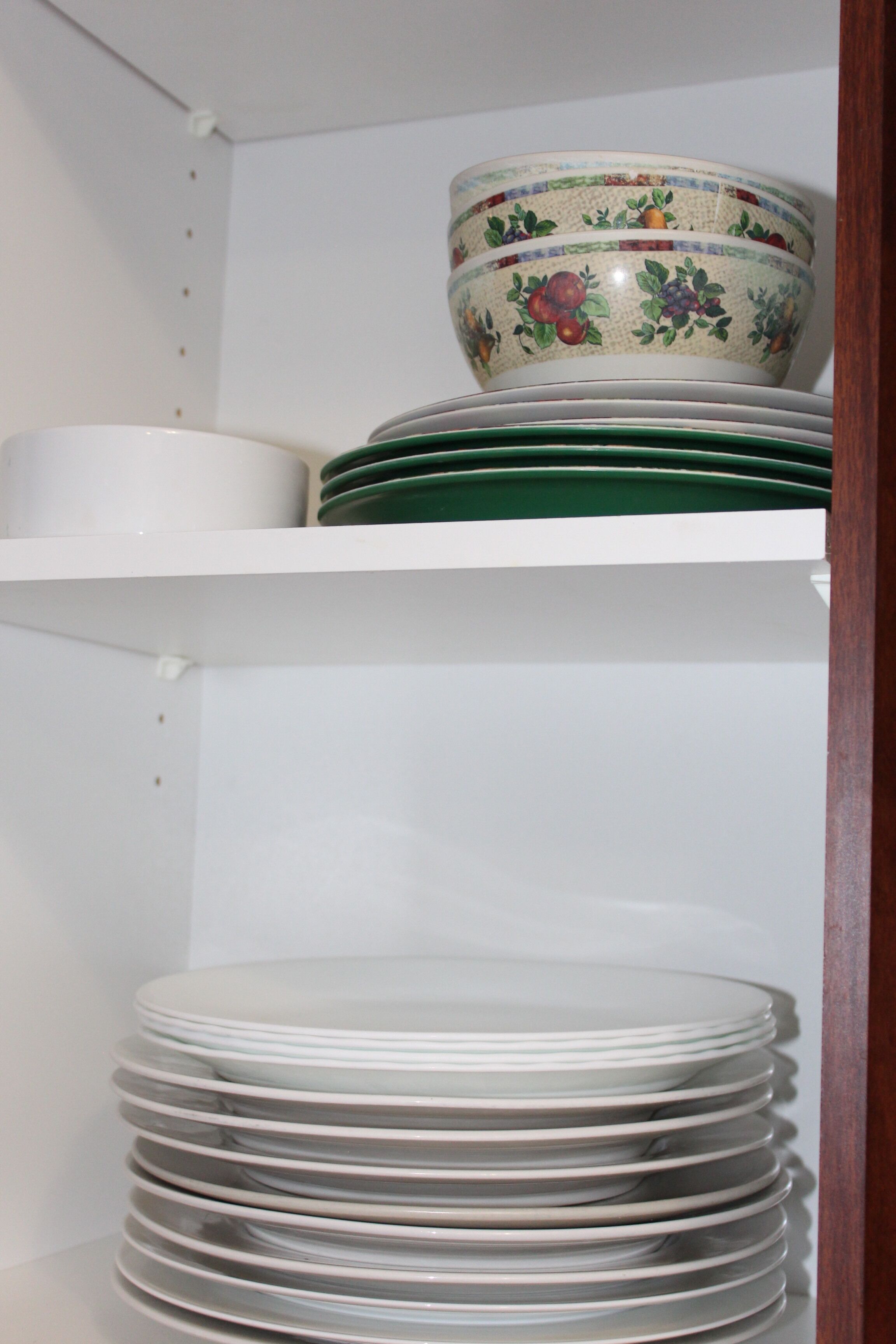 A shelf with stacked white plates and a decorative bowl with fruit patterns.