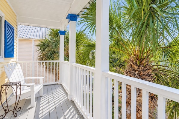 A covered porch with white railings, a bench, and a chair.