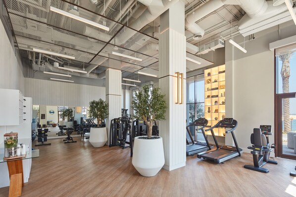 Un gimnasio moderno con equipamiento de ejercicio, ventanas amplias y suelo de madera.