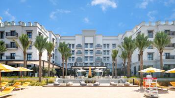 A hotel courtyard with a pool, sun loungers, and palm trees.