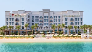 Un hotel grande con varios pisos, balcones y una zona de playa con tumbonas y sombrillas.
