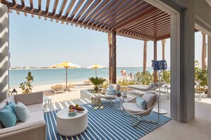Un área de descanso junto a la playa con vista al mar, que incluye un sofá, sillas, una mesa redonda y sombrillas.