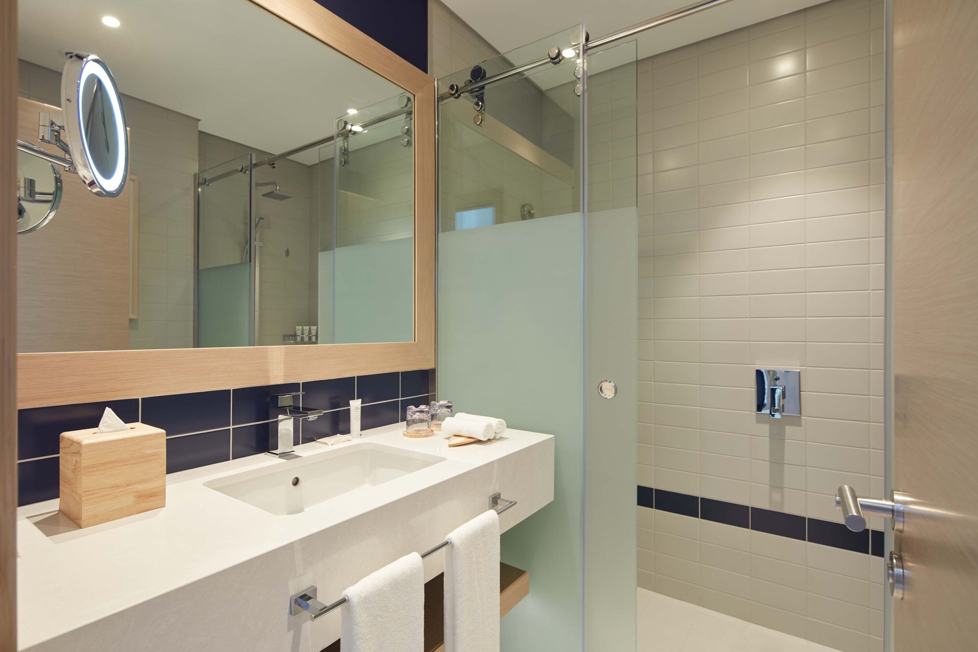 A modern bathroom with two sinks, a large mirror, and a glass shower enclosure.