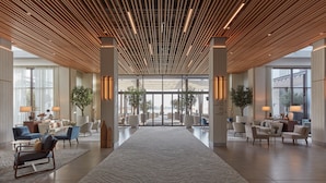 Un hall espacioso con diseño moderno, que presenta un techo de madera, ventanas amplias y zonas de estar cómodas.