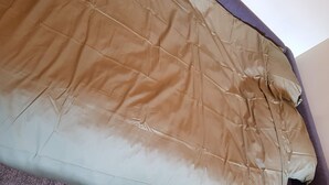 Un lit avec une couette marron et beige, une tête de lit violette et un mur blanc.