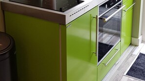 Une cuisine compacte avec un îlot central vert, un four encastré et une fenêtre donnant sur un paysage verdoyant.