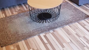 Un salon moderne avec un canapé d’angle gris, une table basse ronde dotée d’un pied en fil métallique et un tapis à motifs.