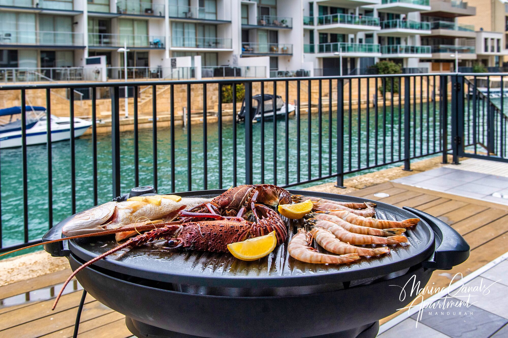 Ein Grill mit Meeresfrüchten auf einem Balkon mit Blick auf einen Yachthafen und Gebäude.