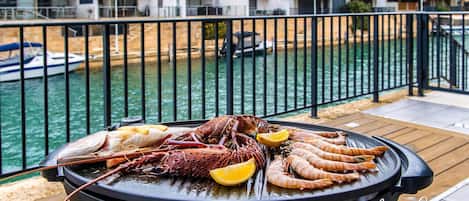 A seafood grill on a balcony with a view of a marina and buildings.