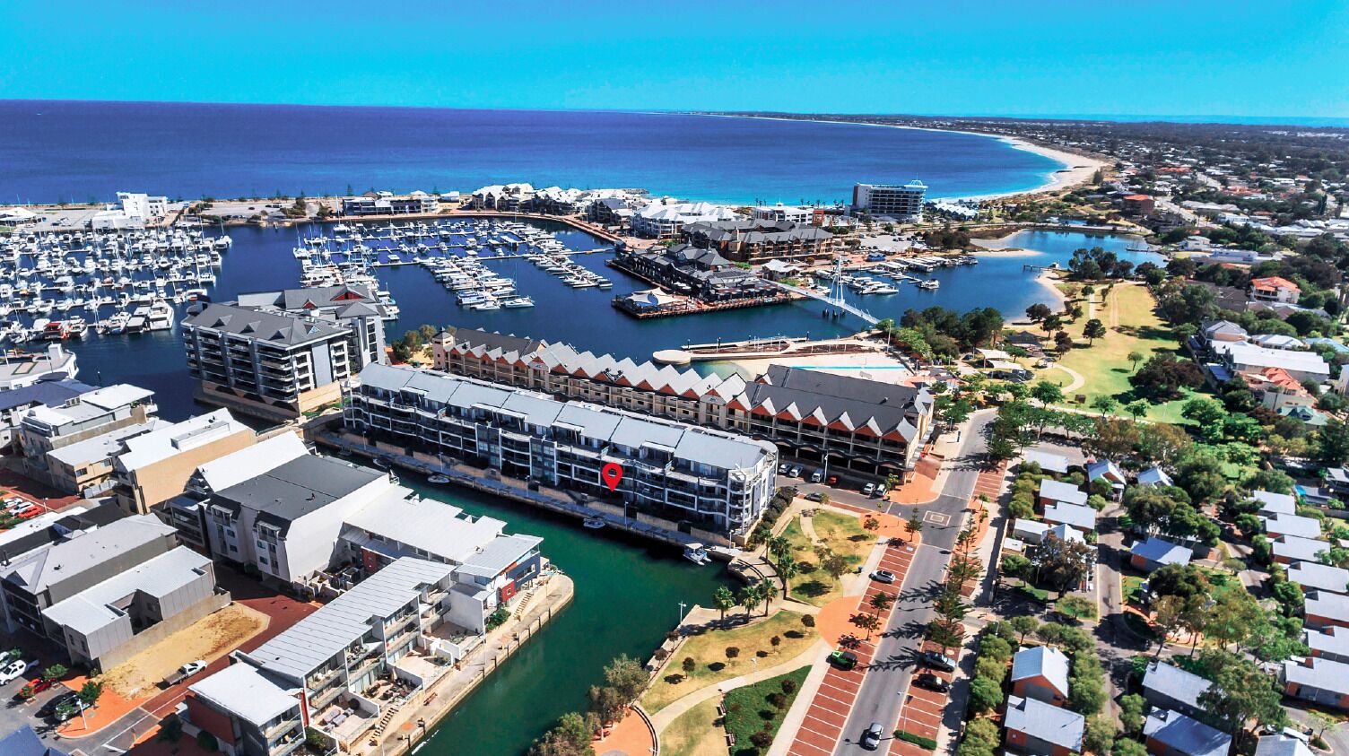 Vue aérienne d’une marina avec des bateaux, un grand bâtiment d’hôtel et les quartiers résidentiels environnants.