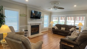 A living room with a fireplace, two sofas, a TV, and a ceiling fan.