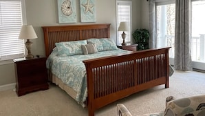 A bedroom with a wooden bed, two bedside tables, a ceiling fan, and a large window with curtains.
