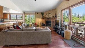 A spacious living area with a fireplace, a large sofa, and a kitchen area with wooden cabinets and large windows. - Great Views, Summer Resort Activities! (Durango)