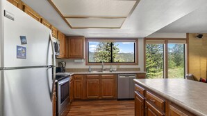 A kitchen with wooden cabinets, a stainless steel refrigerator, a dishwasher, and a window with a mountain view. - Great Views, Summer Resort Activities! (Durango)