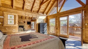 A log cabin bedroom with a large bed, a fireplace, and a balcony with a wooden railing. - ER16 - Mountain Blessing | Great location - Close to town! (Pigeon Forge)