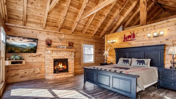A log cabin bedroom with a bed, a fireplace, a mounted TV, and a window. - ER16 - Mountain Blessing | Great location - Close to town! (Pigeon Forge)