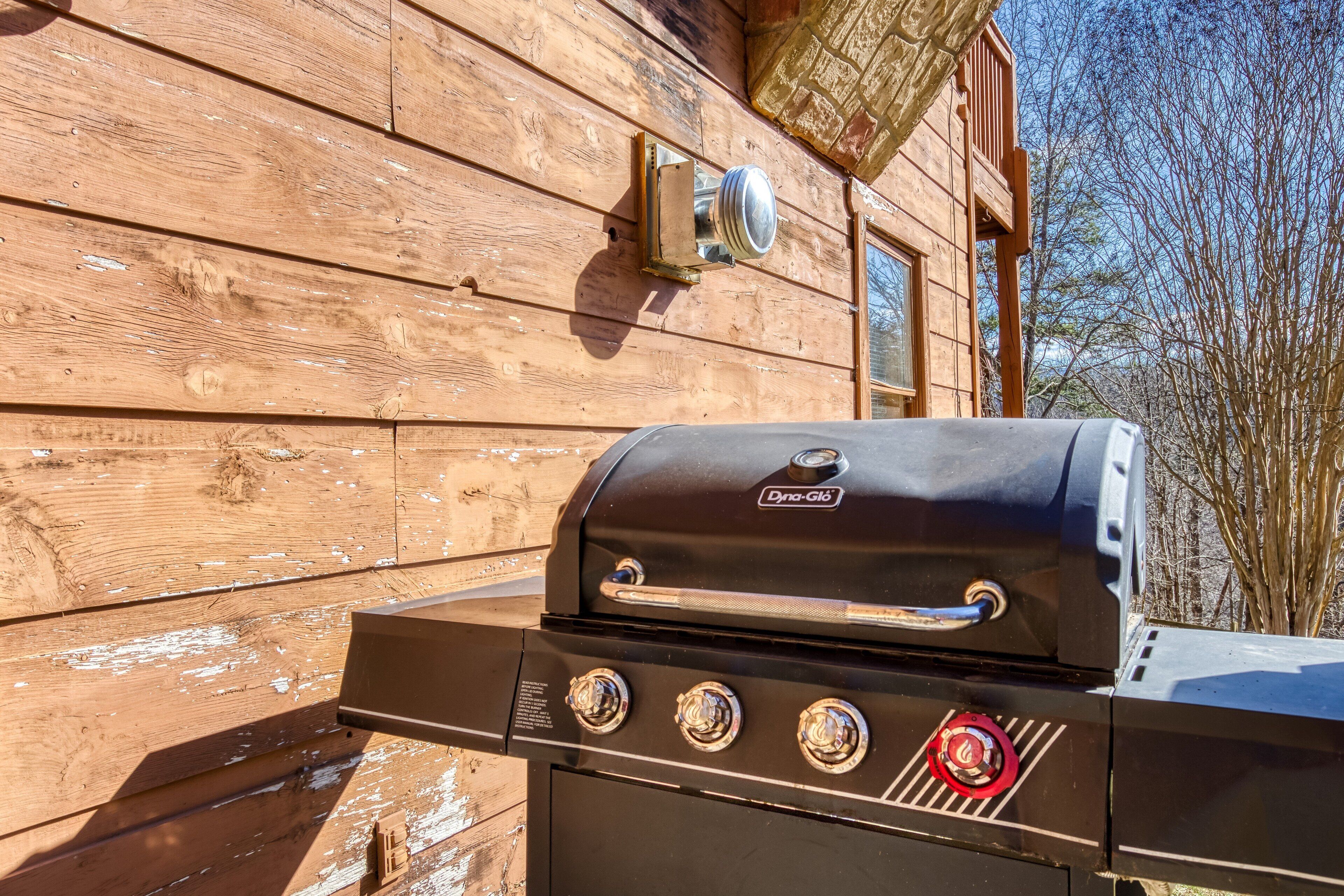 Una parrilla negra para exteriores con la marca 'Dyna-Glo' frente a un muro de cabaña de madera.