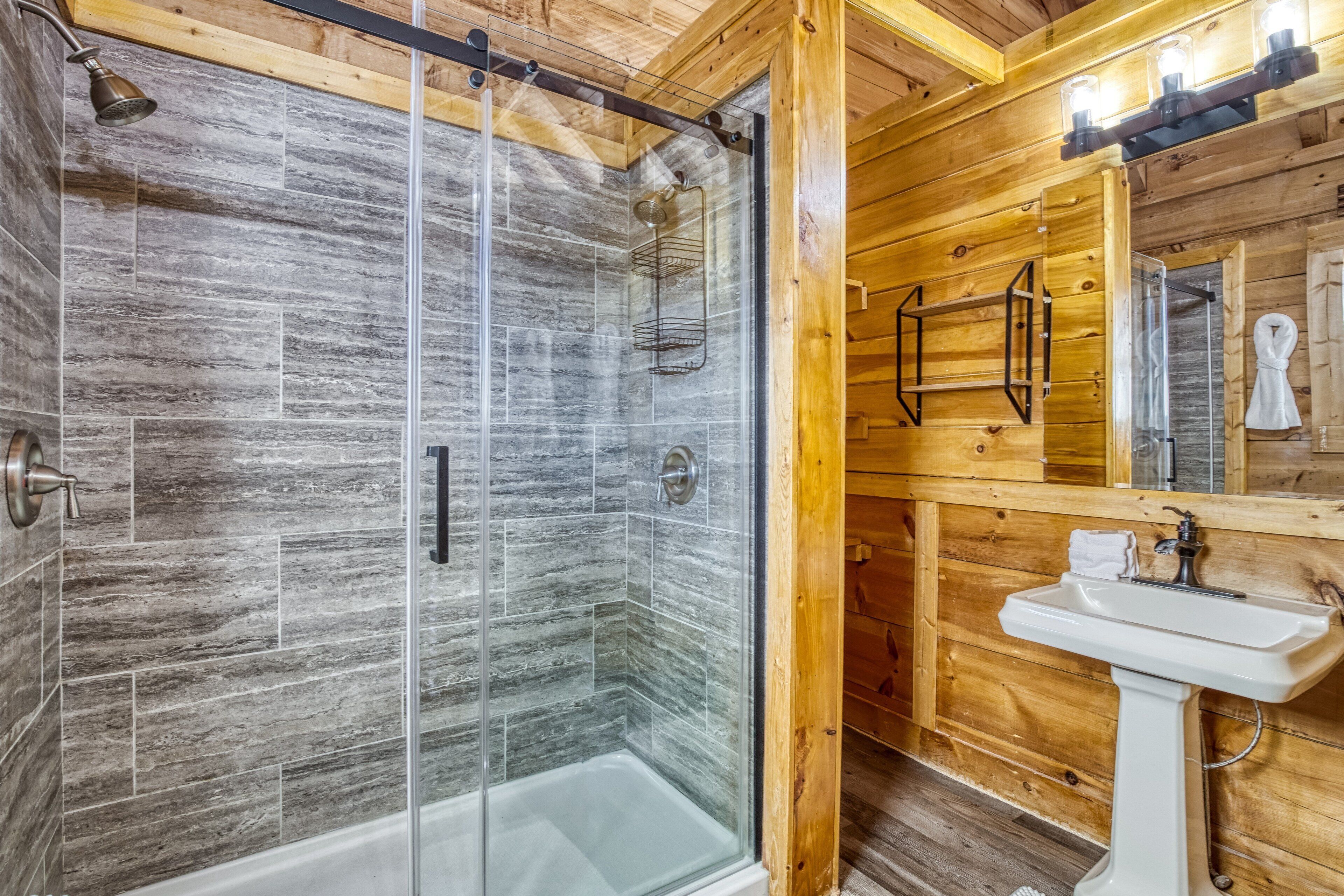 A wooden cabin bathroom with a glass-enclosed shower, a white sink, and a wooden vanity.