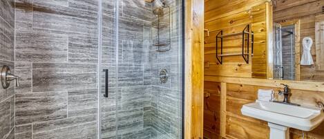 A wooden cabin bathroom with a glass-enclosed shower, a white sink, and a wooden vanity.