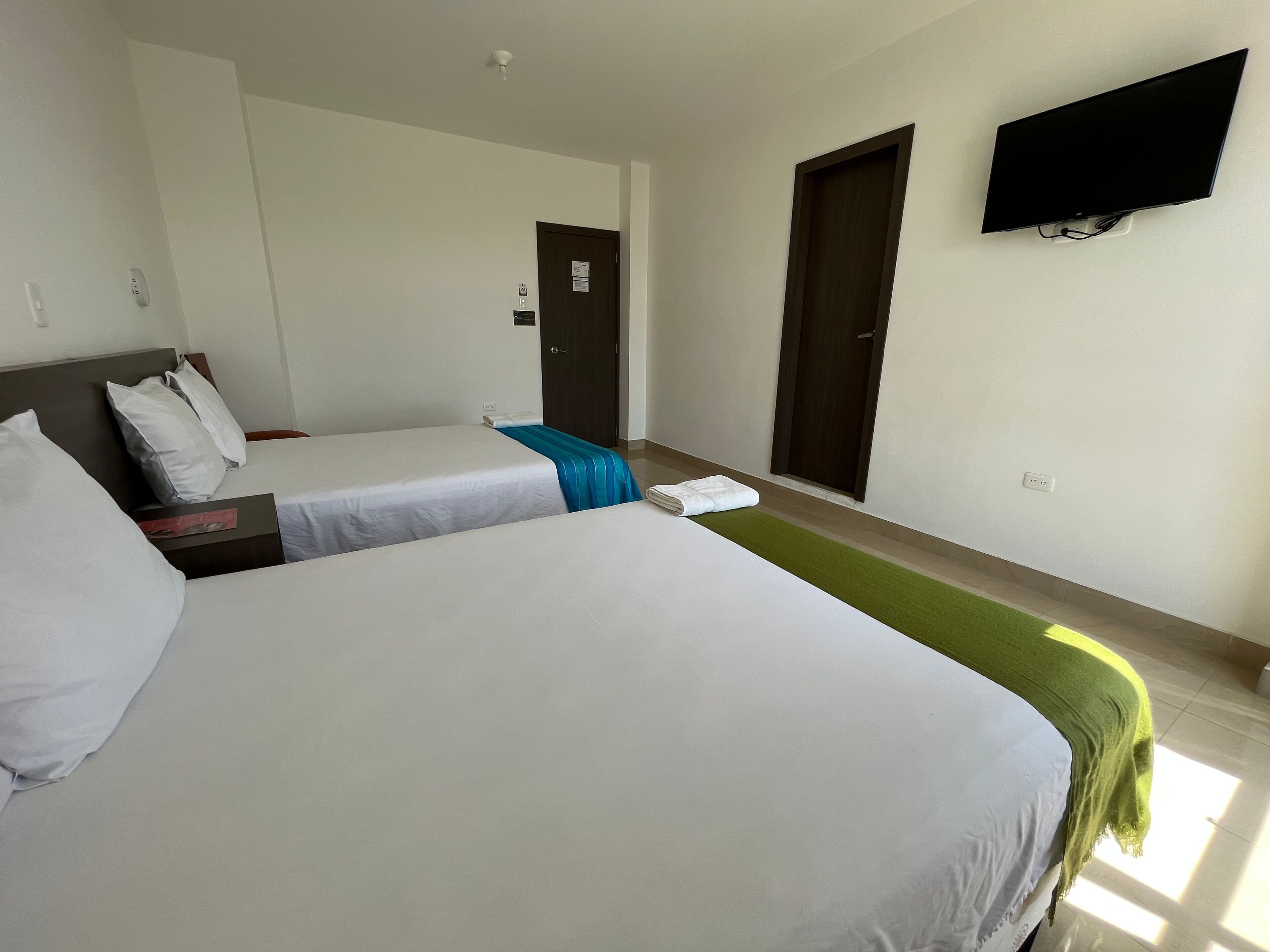 A hotel room with two beds, a flat-screen TV mounted on the wall, and a door with a sign.