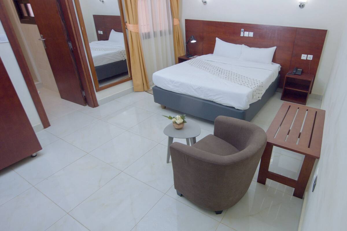 A hotel room with a bed, a chair, a small table, and a nightstand.
