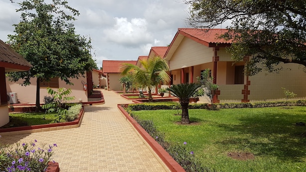 A pathway leading to a row of buildings with red roofs, surrounded by well-maintained greenery and flower beds. - Hôtel La Rose Blanche Korhogo (Korhogo)