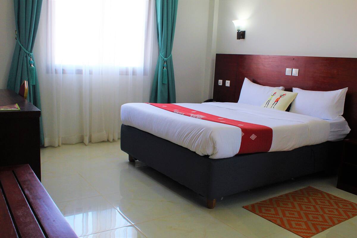 A hotel room with a bed, a wooden bench, a nightstand, and a patterned rug.