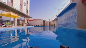 A swimming pool with clear blue water, surrounded by a building with tiled walls and a balcony. - Hôtel La Rose Blanche Korhogo (Korhogo)