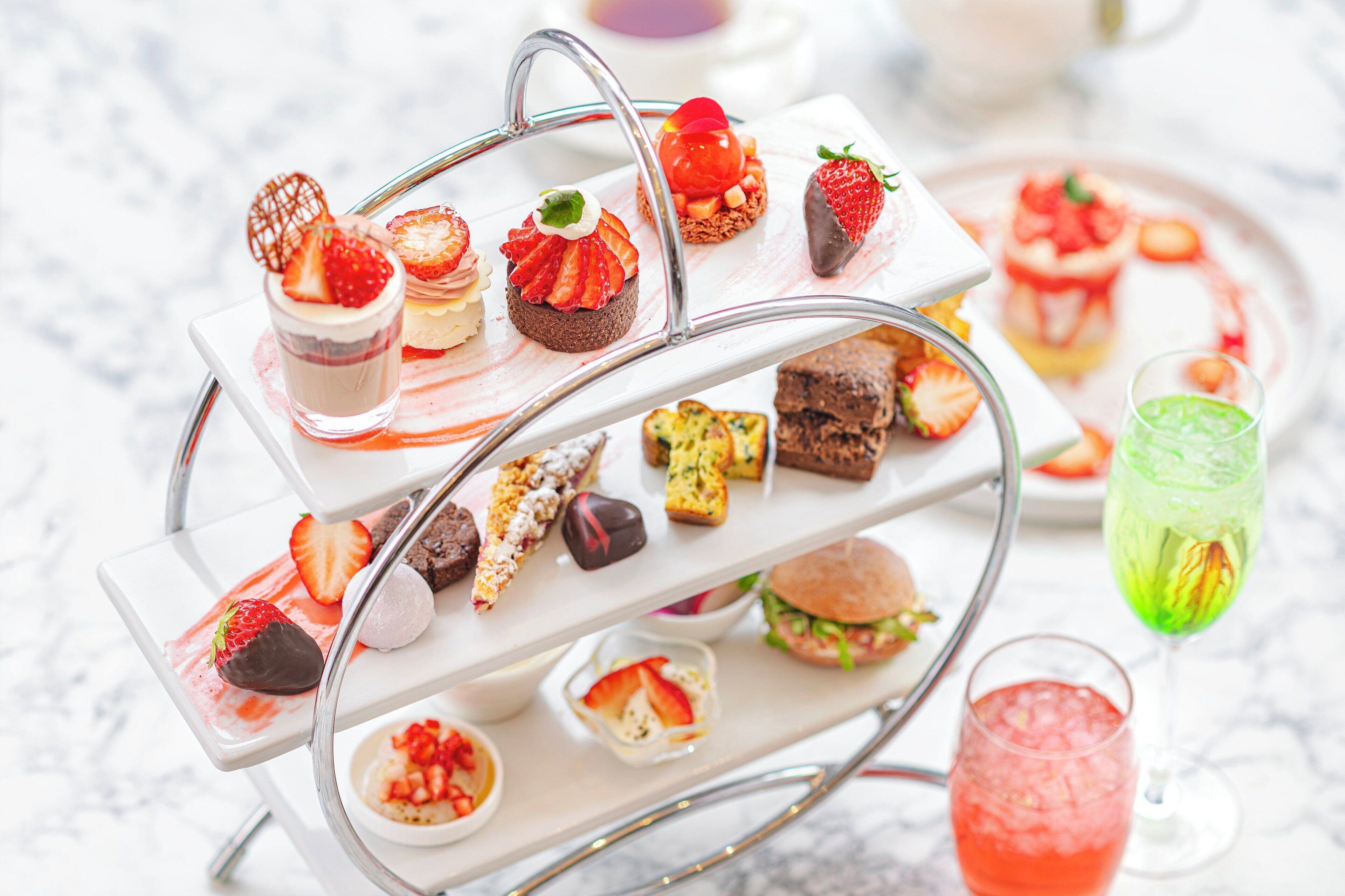 Un présentoir à étages garni de divers desserts et boissons, notamment des fraises, du chocolat et un cocktail vert.
