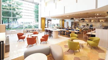 Relax in a spacious public area with round tables and cushioned chairs, offering a view of the outdoors.