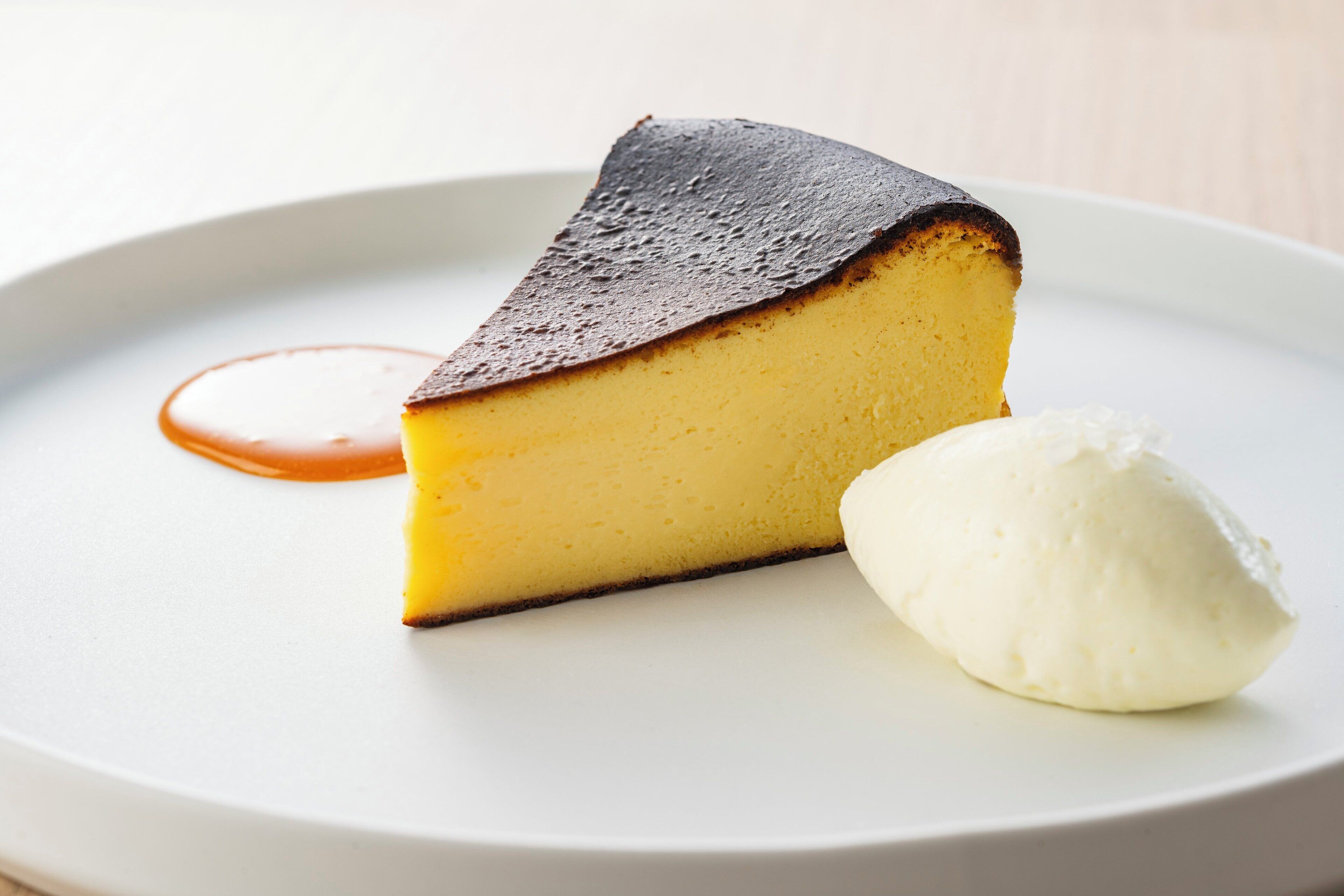 Uma fatia de cheesecake com cobertura caramelizada e uma bola de sorvete de baunilha em um prato branco.