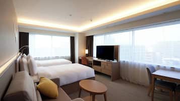 A hotel room with two beds, a sofa, a desk, a TV, and a city view.
