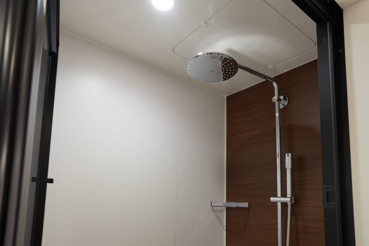 A modern shower with a handheld showerhead, a wall-mounted control panel, and a wooden panel wall.