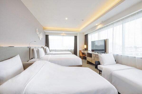 Habitación de hotel con dos camas, un escritorio, televisor y ventana grande.