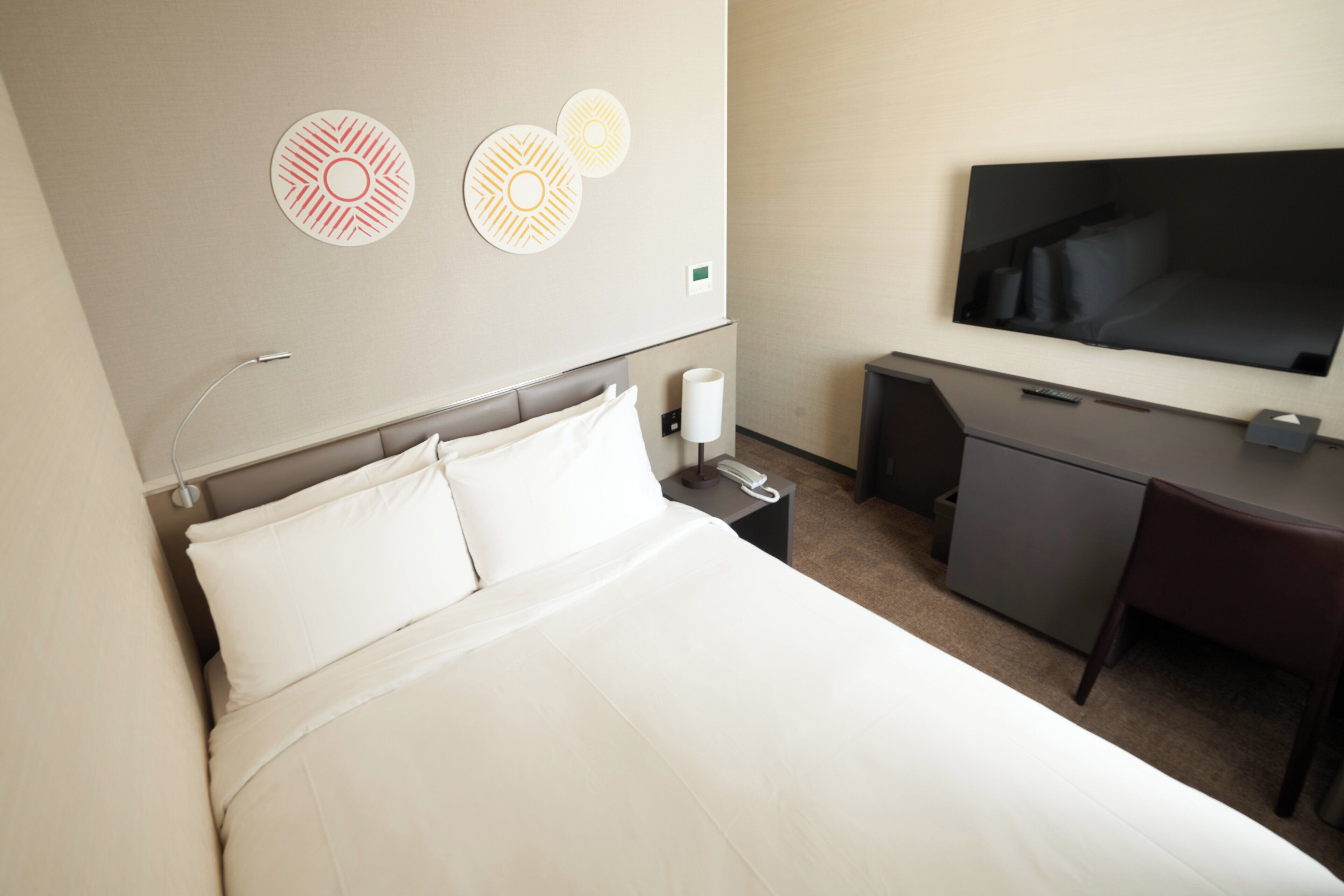 Une chambre d’hôtel équipée d’un lit, d’un bureau, d’une télévision et décorée avec des œuvres d’art mural.