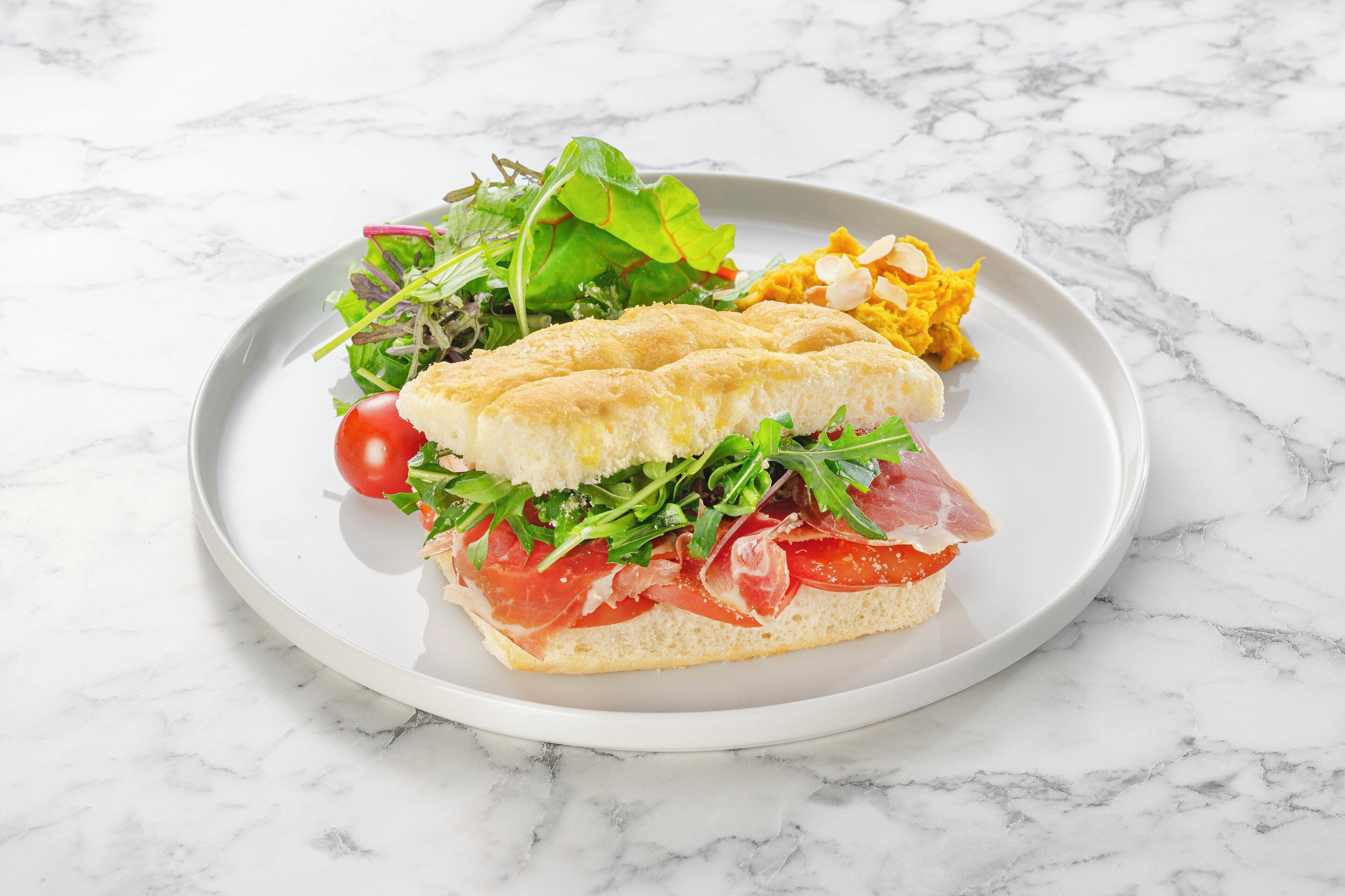 Un sándwich con verduras y carne en un plato, acompañado de una ensalada y papas fritas.