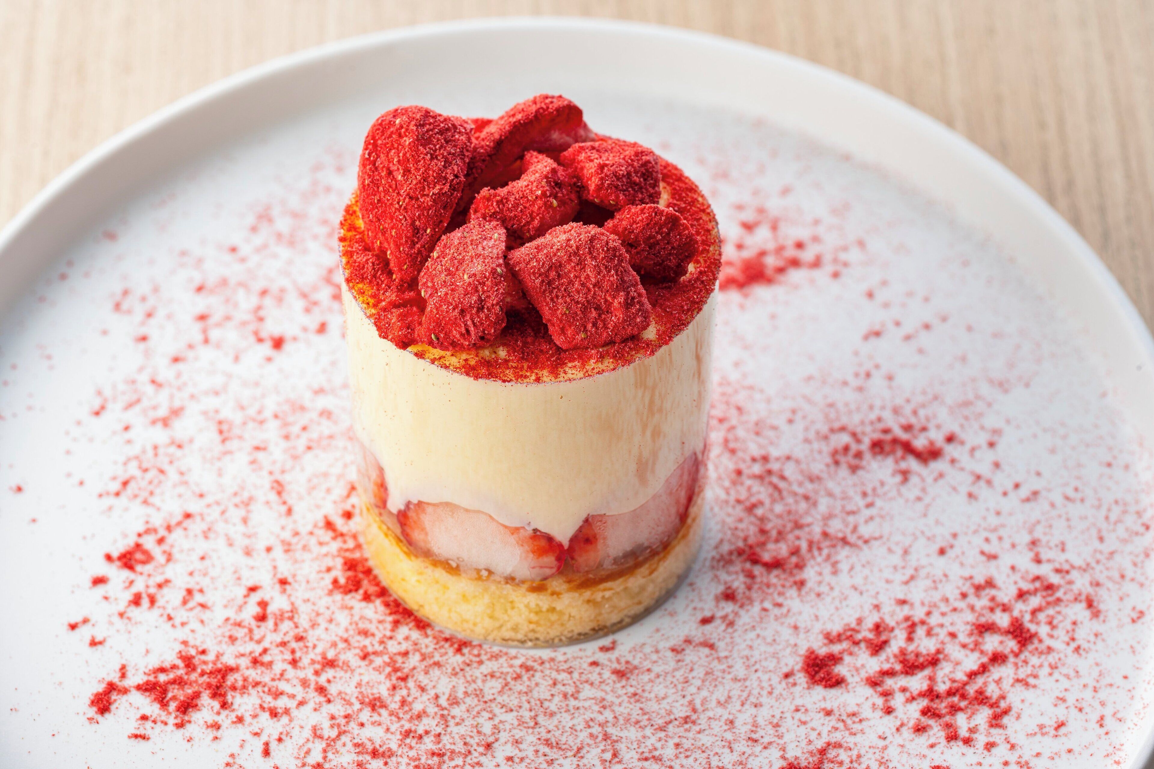 A dessert with a creamy layer, a fruit layer, and a dusting of red powder on a white plate.