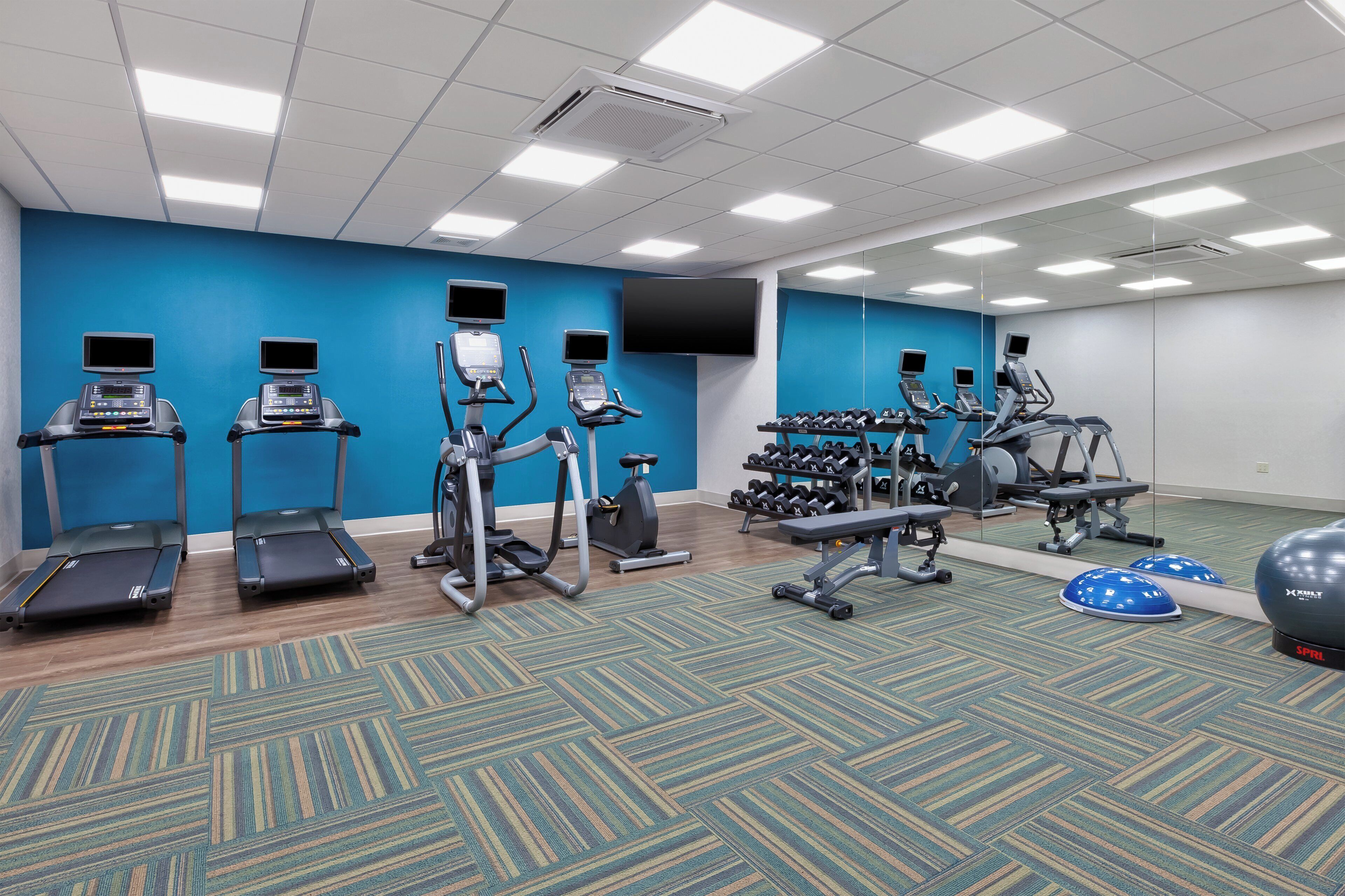 Un gimnasio con cintas de correr, elípticas y pesas libres.