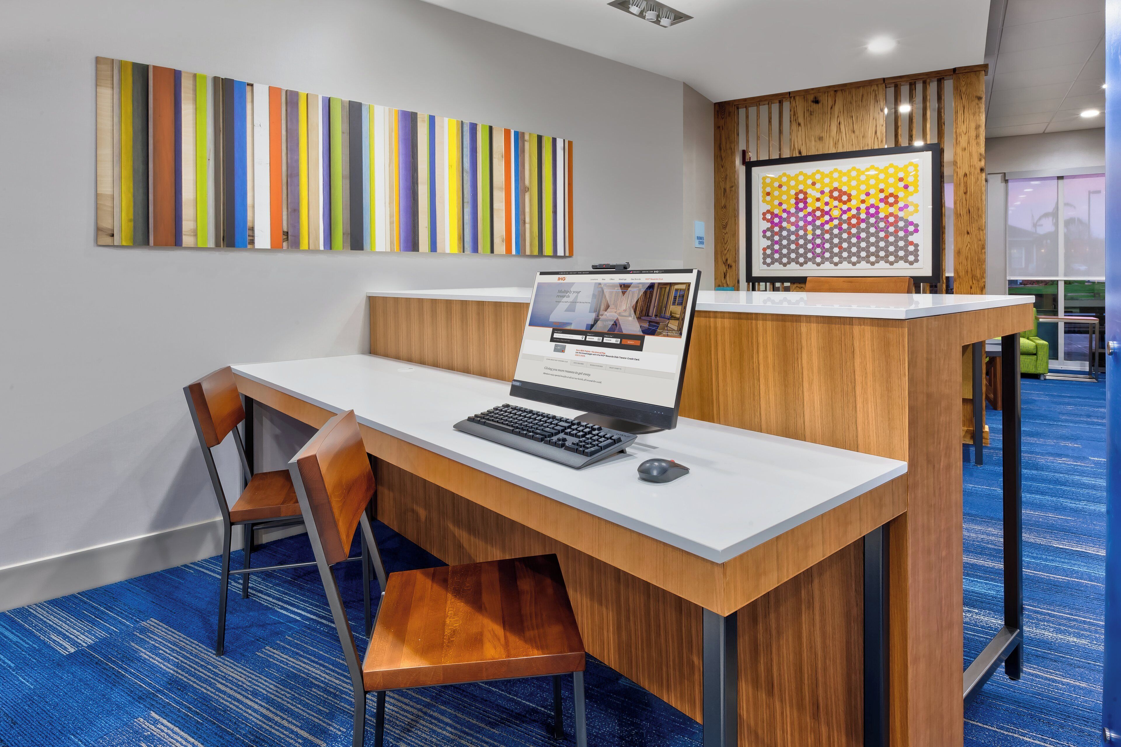 A reception desk with a laptop, a framed artwork, and a seating area with chairs.