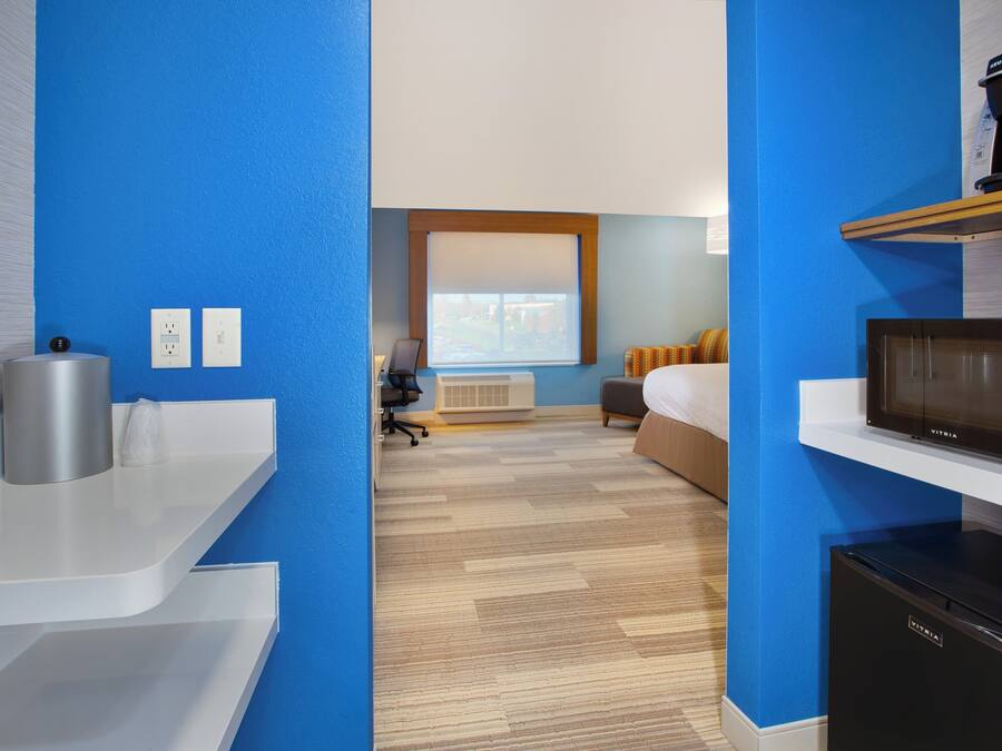 Habitación de hotel con kitchenette, cama, escritorio y ventana con persianas.